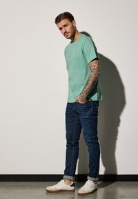 Camiseta de cuello redondo verde menta, jeans de color azul oscuro y zapatillas blancas. La tela es suave, los jeans tienen costuras sutiles y las zapatillas tienen acentos contrastantes.