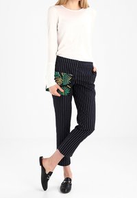 Ljusrosa långärmad topp, svarta randiga byxor och svarta slip-on skor. Innehåller en pärlad grön och svart mönstrad clutch.