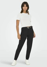 Pantaloni neri su misura con vestibilità slim, dotati di tasche frontali. Abbinati a una maglietta bianca a maniche corte e una cintura nera con fibbia metallica.
