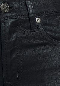 Svarta denimjeans med en glänsande yta, med en metallknapp med "GAP"-logotyp och sydda fickor längs sidorna.