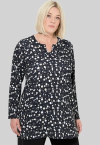 Tunique à manches longues en tissu doux, avec un fond noir et un motif abstrait de cercles blancs et crème, décolleté en V.
