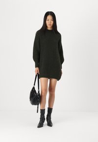 Maglione oversize di colore verde scuro, con texture a coste e spalle scese. Abbinato a una borsa nera e stivali con tacco.