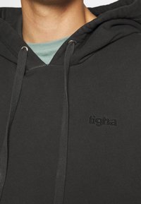 Hoodie nero realizzato in tessuto morbido, con tasca frontale, cordini e logo in rilievo. Il colletto interno presenta un colore blu-verde a contrasto.