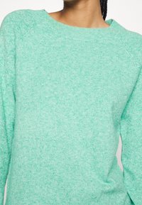 Hellgrüner Strickpullover mit rundem Ausschnitt und Raglanärmeln, mit weicher Textur und dezentem gesprenkeltem Muster.