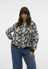 Chaqueta bomber negra con estampado floral blanco, cierre de cremallera, puños y dobladillo acanalados, con un corte relajado y textura de tela suave.