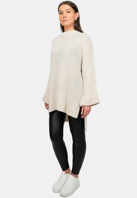 Lichtbeige gebreide sweater met brede mouwen, een high-low zoom, textiel stof, gecombineerd met zwarte legging en witte sneakers.