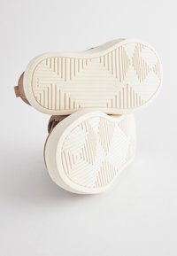 Sneakers met een gestructureerde bruine bovenkant, crèmekleurige rubberen zool met een geometrisch patroon, afgeronde vorm en zonder zichtbare merk- of accentdetails.