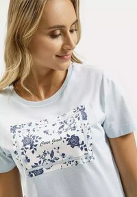 Jasnoniebieska koszulka z krótkim rękawem z floralnym nadrukiem w granatowym kolorze z przodu, z tekstem "Cross Jeans" wkomponowanym w projekt.