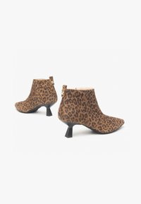 Stivaletti alla caviglia in pelle scamosciata con stampa leopardata, dotati di punta affusolata e un originale tacco a blocco. Gli accenti dorati sul retro aggiungono un tocco di dettaglio.