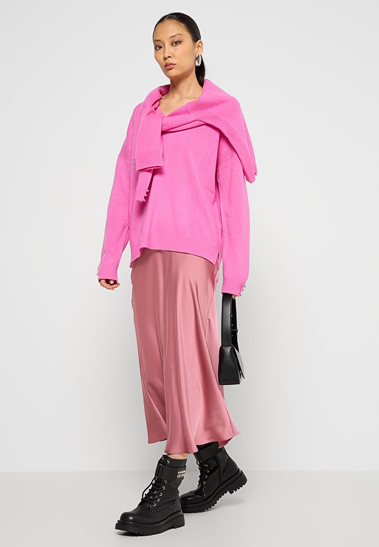 Suéter de punto rosa superpuesto a una falda de satén rosa, combinado con botas negras con cordones y un pequeño bolso negro. Texturas suaves y colores audaces.