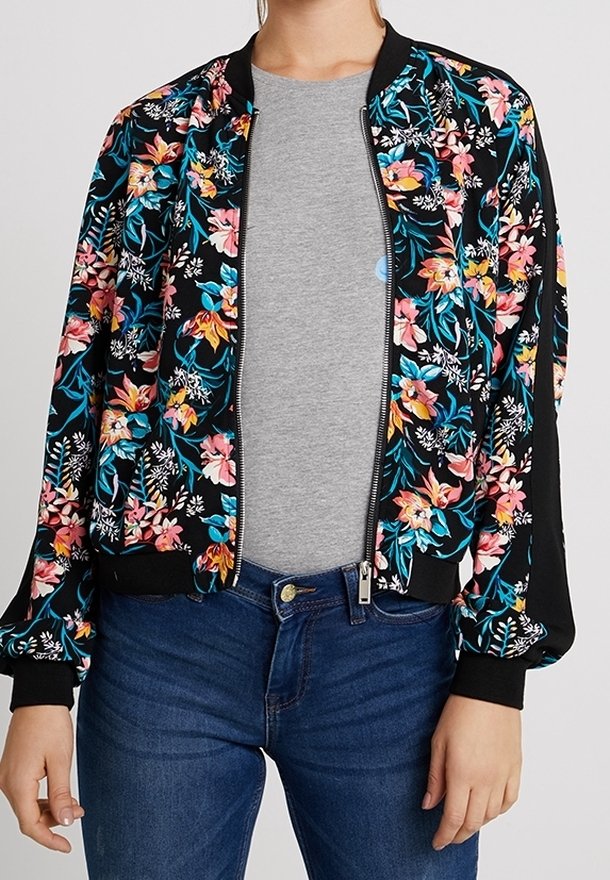 Blumiger Bomberjacke mit schwarzem Grundton und bunten Mustern in Pink, Blau und Weiß, mit Reißverschluss vorne und gerippten Bündchen und Saum. Getragen über einem grauen Oberteil.