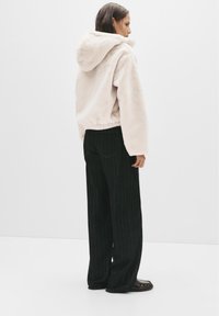 Hoodie in finta pelliccia rosa chiaro con cordino, abbinato a pantaloni a gamba larga a righe neri. Presenta una vestibilità comoda e una vita elasticizzata.