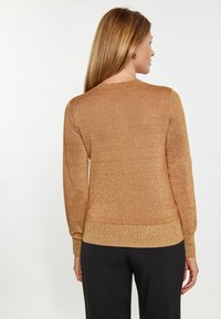 Goldener Glitzerpullover mit langen Ärmeln und Rundhalsausschnitt, mit einem taillierten Saum. Glatte Textur, lichtreflektierendes Material und keine sichtbaren Muster.
