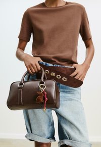 Brun læderhåndtaske med rund form, sølvhardware og en kanin-nøglering. Båret med et brunt bælte og lyseblå, baggy denimshorts.