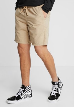 Shorts en coton beige avec une taille élastique et un cordon de serrage, associés à des baskets montantes à carreaux noir et blanc.
