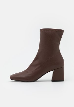 Botte en cuir marron mi-mollet avec bout carré et talon bloc, texture lisse et bord supérieur cousu.