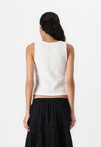 White sleeveless top with vertical ribbed texture and scalloped edge at the neckline, paired with a flowing black skirt.