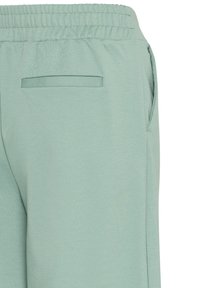 Lichtgroene sportieve broek met een elastische tailleband, zijzak en een gladde textuur. Het ontwerp is minimalistich met een achterzakdetail.