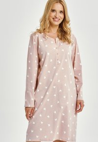 Miękka różowa koszula nocna z długimi rękawami, z zapięciem na guziki przy dekolcie i wzorem białych serc. Tkanina wydaje się gładka i lekka.