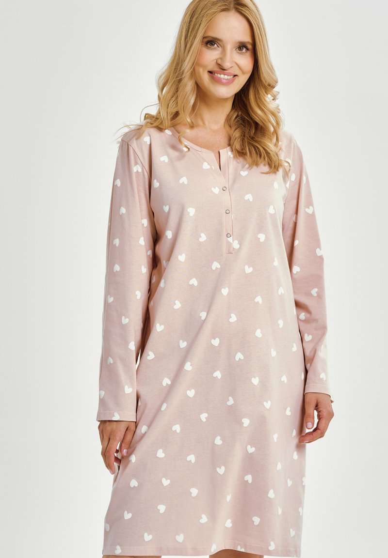 Miękka różowa koszula nocna z długimi rękawami, z zapięciem na guziki przy dekolcie i wzorem białych serc. Tkanina wydaje się gładka i lekka.