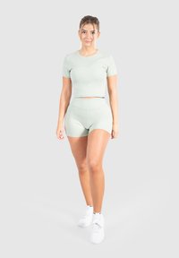 Completo sportivo verde chiaro composto da una maglietta aderente a maniche corte e pantaloni corti a vita alta, entrambi realizzati in un tessuto liscio e elastico. Sneakers bianche.