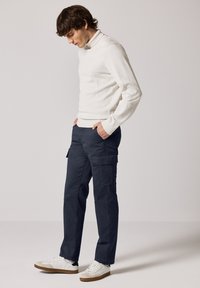 Light gray sweater with a high collar, navy cargo pants featuring side pockets, and white sneakers with tan accents.
