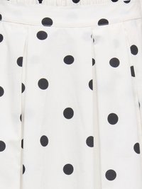 Tissu blanc à pois noirs, avec des plis et une couture visible sur la partie supérieure.