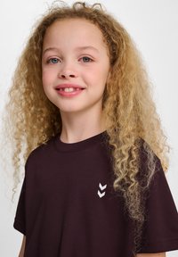 Bordowa koszulka z krótkim rękawem, z białym wzorem w zygzak po lewej stronie. Wykonana z gładkiego, miękkiego materiału.