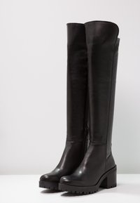 Botas negras hasta el muslo hechas de cuero liso con un tacón grueso de plataforma, con cremallera lateral y suela texturizada para una mejor tracción.