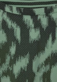 Primo piano di un tessuto con un motivo astratto verde e nero e una sottile texture a pois visibile sulla superficie.