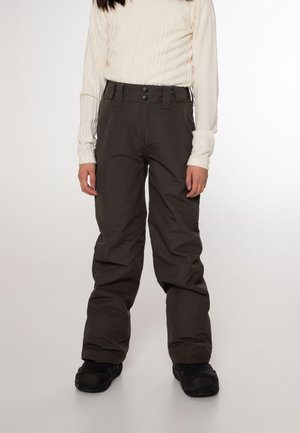 Persoon draagt zwarte sneeuwbroek met dubbele knoopsluiting en zwarte laarzen, gecombineerd met een crèmekleurige geribbelde top met lange mouwen.