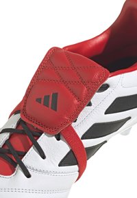 Scarpa da calcio bianca e rossa con una tomaia in pelle texturizzata, dettagli neri e una linguetta imbottita con un motivo a diamante.