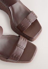 Sandales compensées en cuir marron avec larges brides présentant des détails cousus et bouts carrés sur semelles plateforme texturées.