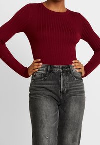 Haut à manches longues bordeaux côtelé avec un col rond, associé à un jean en denim gris taille haute présentant un léger délavage et des distresses.