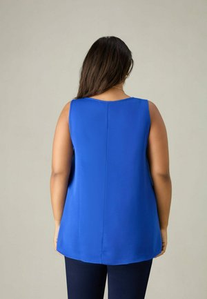 Blauw mouwloos topje van soepel materiaal, met een ronde halslijn en een rechte rugontwerp, gecombineerd met donkere broeken.
