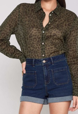 Khaki luipaardprint blouse van doorschijnende stof met knopen, gecombineerd met hooggetailleerde blauwe denimshorts met opgerolde pijpen en achterzakken.