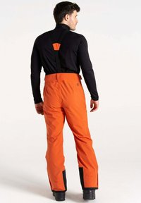 Wasserdichte orange Skihosen mit verstellbaren schwarzen Trägern, verstärkten schwarzen Bündchen und einer glatten Textur. Entworfen für Outdoor-Aktivitäten.