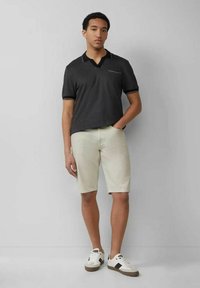 Dunkelgraues Polohemd mit Kragen und Taschenübersicht, kombiniert mit hellbeigen Shorts und weißen Sneakers mit schwarzen Akzenten.
