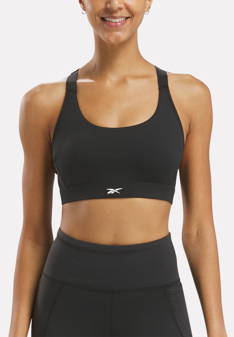 Sujetador deportivo negro hecho de material elástico, con cuello en forma de scoop, tirantes anchos y un logo blanco en la banda delantera.