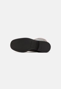 Semelle extérieure en caoutchouc noir avec une surface lisse, un bord incurvé et un léger motif de traction. Marque minimale près de la zone du talon.