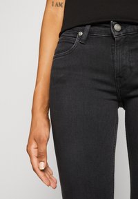 Jeans de mezclilla negra con un diseño ajustado, que cuentan con un cierre clásico de botón y cremallera. Textura suave y un sutil detalle de costura.