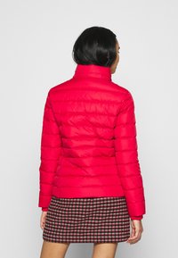 Czerwona ocieplana kurtka z wysokim kołnierzem, pikowana, dopasowana. Noszona na wzorzystą spódnicę, kładąc nacisk na ciepło i komfort.