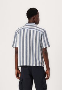 Camisa de manga corta con rayas verticales azules y blancas, que presenta una tela texturizada y un bolsillo de parche en el lado izquierdo.