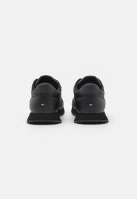 Scarpe da ginnastica nere con tomaia in pelle liscia, suola in gomma testurizzata e un piccolo dettaglio del logo sul tallone. Design a bassa altezza.