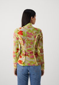 Blomstret langærmet top i gennemsigtigt stof med pink, orange og grønne mønstre. Rynkede detaljer langs sømmene fremhæver teksturen.
