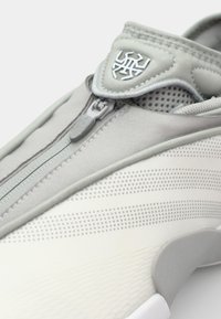 Sneaker med en grå tekstiloverdel med lynlås, perforerede paneler og en struktureret hvid sål. Inkluderer et logo på anklen.