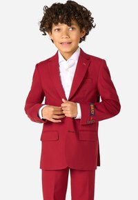Blazer rosso con due tasche frontali e rever a V, abbinato a una camicia bianca. I polsini presentano un motivo ricamato "DAILY" in blu.