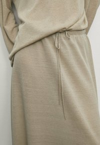 Beige gestricktes Kleid mit lockerer Passform, das eine Kordelzugtaille und eine weiche Textur aufweist. Einfaches Design und lange Ärmel.