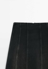 Jupe en jean noire avec des coutures verticales et une taille haute sur fond blanc.