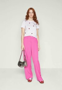 Camiseta blanca a rayas con patrones de corazones rojos, combinada con pantalones de pierna ancha de color rosa brillante. Lleva un bolso plateado y calza zapatos marrones y de colores.